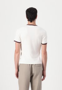 Short-sleeved cream t-shirt featuring a dark brown ribbed collar and sleeve edges, made of soft cotton blend fabric, fitted design.