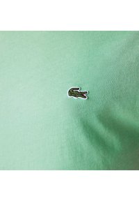 Groene katoenen T-shirt met een klein geborduurd krokodillenlogo in zwart en rood. Gladde textuur en ronde halslijn.