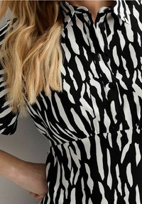 Černobílé šaty se zebrovým vzorem, krátké rukávy, knoflíková léga a přiléhavý pas. Hladká textilie.