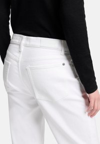 Jeans di denim bianco con vita alta, dotati di due tasche posteriori e un'etichetta in pelle in vita. Il tessuto ha una superficie liscia.