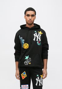 Czarna bluza z kapturem z haftowanym logo New York Yankees, kolorowymi naszywkami, w tym Statua Wolności, gwiazdy i kości do gry. Konstrukcja z kieszenią typu kangur.