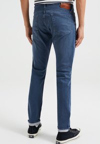 Granatowe dżinsy o prostym kroju, z skórzaną łatą w pasie, pięcioma kieszeniami i podwiniętymi mankietami. W połączeniu z czarnymi trampkami.