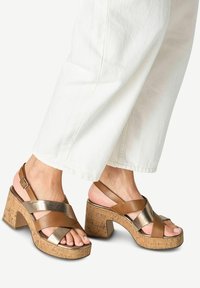 Bruna sandaler med remmar och metalliska detaljer samt en klack i kork. Har ankelremmar och en korsad design för både stöd och stil.