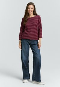 Haut à rayures bordeaux à manches longues associé à un jean en denim foncé à jambes larges et des baskets blanches. Le haut présente un décolleté bateau et un tissu doux.