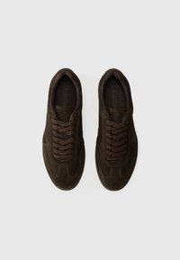 Zapatillas de ante marrón oscuro con forma redondeada, paneles texturizados y cordones marrones. Las suelas de goma y los sutiles detalles de costura completan el diseño.