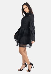 Zwarte jurk met lange mouwen, aansluitend lijfje, kantdetails en een gelaagde rok. Draag met zwarte hoge hakken sandalen.