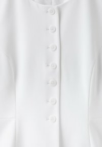 Vêtement blanc avec une rangée de huit boutons blancs courant verticalement au centre devant.
