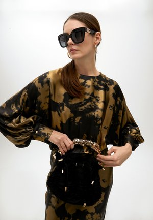 Robe tie-dye noire et dorée avec des manches volumineuses, associée à des lunettes de soleil oversize noires et un sac à main texturé noir avec une poignée en imprimé léopard.