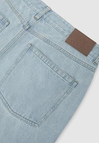 Poche arrière de jean en denim bleu clair avec surpiqûres beiges et étiquette en cuir marron à la taille.