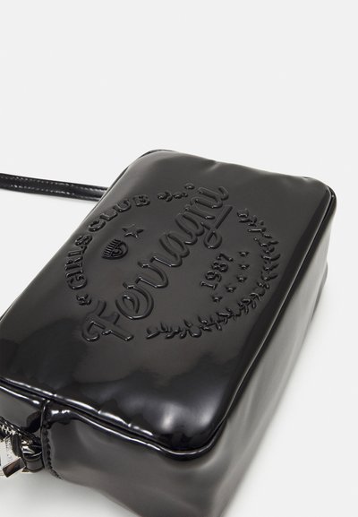 Glatte schwarze rechteckige Umhängetasche mit geprägtem Text "Fiorucci Girls Club 1987" sowie dekorativen Sternen und Blättern auf der Vorderseite.