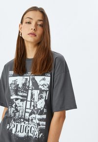 Grijze oversized t-shirt van katoen, met een grafisch ontwerp van stadsgezichten en muziekafbeeldingen in zwart-wit, geaccentueerd door vetgedrukte tekst.