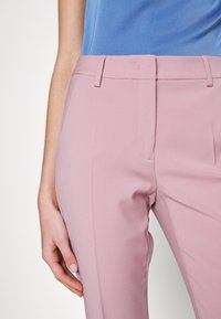 Jasnoróżowe spódnie o dopasowanym kroju, z gładką fakturą, z płaskim przodem i pętlami na pasek. Całość uzupełnia niebieska bluzka.