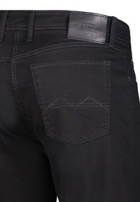 Des jeans en denim noir présentent une texture lisse, une coupe droite, des poches arrière distinctives avec un point zigzag, et une étiquette en cuir à la taille.