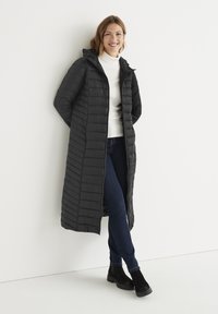 Lang sort pufferjakke med hætte, der har et vandret quiltet design og en frontlynlås. Sættes sammen med blå jeans og sorte ankelstøvler.