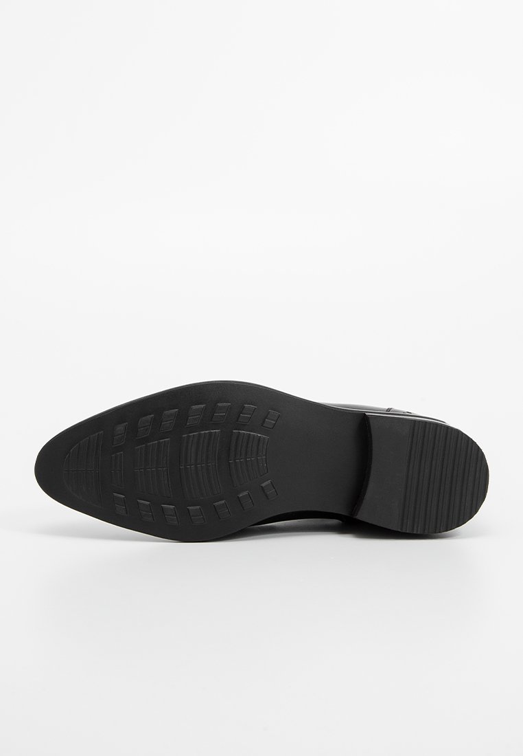 Schwarze Schuhsohle aus strukturiertem Gummi, mit horizontalen und vertikalen Mustern, runder Zehenform und leichtem Absatz.