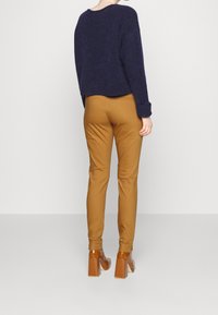 Marinblå kort tröja i fluffig textur. Tan, slim-fit byxor i slät material. Bruna, rejäla klacksandaler med glänsande yta och krokodilmönster.