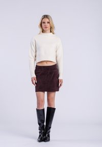 Pull crème court avec ourlet côtelé, associé à une mini-jupe en daim bordeaux foncé. Des bottes noires en cuir lisse, montantes jusqu'aux genoux, complètent le look.
