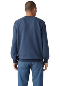 Marineblauwe sweatshirt van zacht materiaal, met ribgebreide boorden en onderkant, ronde halslijn en een losse pasvorm. Gedragen met lichtblauwe jeans.