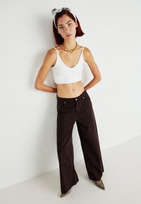 Top scurt alb, blugi maro cu talie înaltă și pantofi cu toc ascuțit metalici. Colier aurit masiv și bentiță cu model pentru accent.