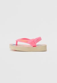Tongs roses avec une semelle intérieure texturée et une épaisse semelle en caoutchouc beige. La lanière arbore le nom de la marque en lettres orange.