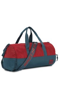 Bolsa de deporte roja y verde azulado hecha de nailon, con dos asas de transporte y correa para el hombro ajustable, que cuenta con un logo de marca y cierre de cremallera.