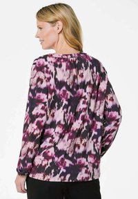 Langarmbluse aus leichtem Stoff mit einem lila und rosa Blumenmuster auf dunklem Hintergrund. Rundhalsausschnitt mit sanften Fältchen im Rücken.