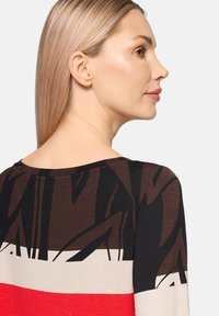 Wielokolorowa bluzka z długim rękawem z brązowym i czarnym abstrakcyjnym wzorem, okrągłym dekoltem i gładką fakturą z intensywnymi czerwonymi i kremowymi akcentami.