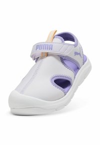 PUMA barn sandaler i vitt och lila med ett kardborreband, meshdetaljer och en vadderad vit sula. Har utskurna sektioner.