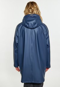 Tamsiai mėlynas vandeniui atsparus paltas su kapišonu, pasižymintis lygiu paviršiumi ir laisvu siluetu. Matomas siuvimas ir prekės ženklo etiketė prie kaklo.