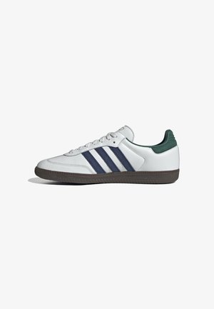 Fehér sneaker tengerészkék csíkokkal és zöld sarkú pöndökkel. Bőrből készült, texturált gumitalppal és kontrasztos varrással.