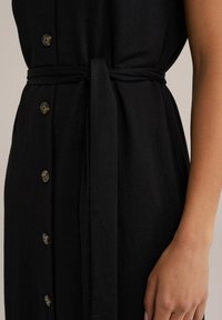 Vestito nero con bottone frontale, cintura in tessuto in vita e maniche corte. Tessuto morbido con una vestibilità rilassata e finitura liscia.