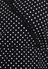 Czarna tkanina w białe kropki, z wypukłym koronkowym wykończeniem wzdłuż krawędzi. Materiał wygląda na miękki i lekki.