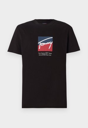 Camiseta de algodón negra con un logo cuadrado en azul y rojo con "Tommy" en escritura blanca, junto con texto en blanco debajo. Mangas cortas.
