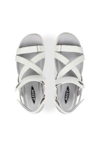 Chanclas de cuero blanco con tiras entrelazadas, hebillas ajustables y una suave plantilla gris. Suela plana y logo de MBT visible.
