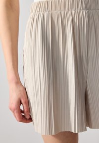 Shorts plissés beige avec une taille élastique. Tissu léger avec des rayures verticales et une texture douce, se terminant juste au-dessus du genou.