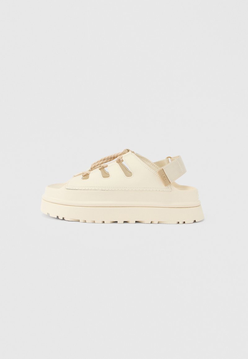 Μπεζ σανδάλι με επίπεδη πλατφόρμα, ανοιχτό δάχτυλο και πλεγμένα κορδόνια. Κατασκευασμένο από ομαλό υλικό με υφασμένο πέλμα και ρυθμιζόμενο λουράκι.