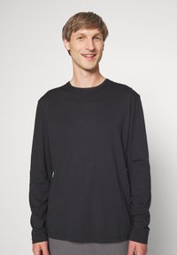 Schwarz langärmliges T-Shirt aus weicher Stoff. Hat einen runden Ausschnitt und einen lockeren Schnitt, mit einer glatten Textur und ohne sichtbare Muster.