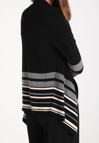 Cardigan lavorato a maglia nero con un orlo alto-basso e strisce orizzontali grigie e rosa. Tessuto morbido, vestibilità rilassata con apertura frontale.