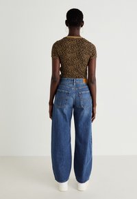 Ruskea leopardi-kuvioinen lyhythihainen paita ja korkeavyötäröiset vaaleansiniset leveät farkut, joissa on kaksi takataskua ja vaaleat kengät.