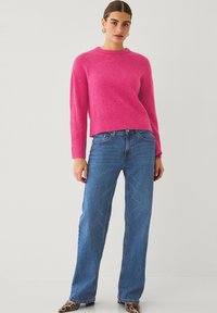 Světle růžový pletený svetr s kulatým výstřihem, doplněný o světle modré volné kalhoty. Outfit se vyznačuje jemnými žebrovanými detaily a uvolněným střihem.