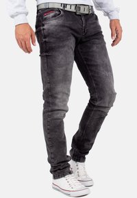 Jeans in denim grigio slim-fit con una leggera lavatura sbiadita, cuciture decorative e passanti per cintura, abbinati a sneaker bianche.
