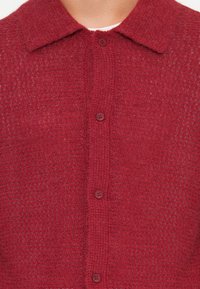 Red knitted cardigan featuring a textured pattern, buttoned front with matching buttons, and a classic collar design.
