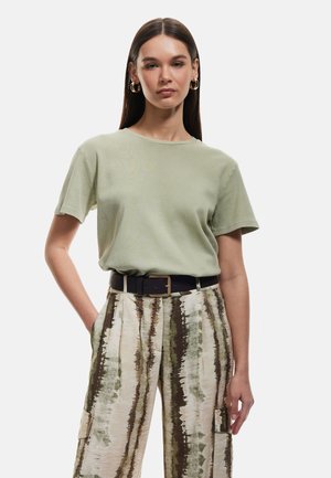 Maglietta in cotone verde chiaro con scollatura rotonda, abbinata a pantaloni cargo a righe verticali beige e verdi e una cintura nera.