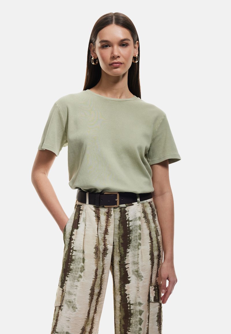 Lichtgroene katoenen t-shirt met een ronde halslijn, gecombineerd met verticaal gestreepte beige en groene cargobroek en een zwarte ceintuur.