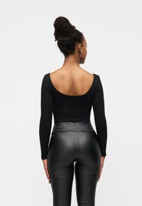 Μαύρο κορμάκι με μακριά μανίκια και ανοιχτή πλάτη, σε συνδυασμό με μαύρο κολάν από ψεύτικο δέρμα με ψηλή μέση, με λεία, γυαλιστερή υφή.