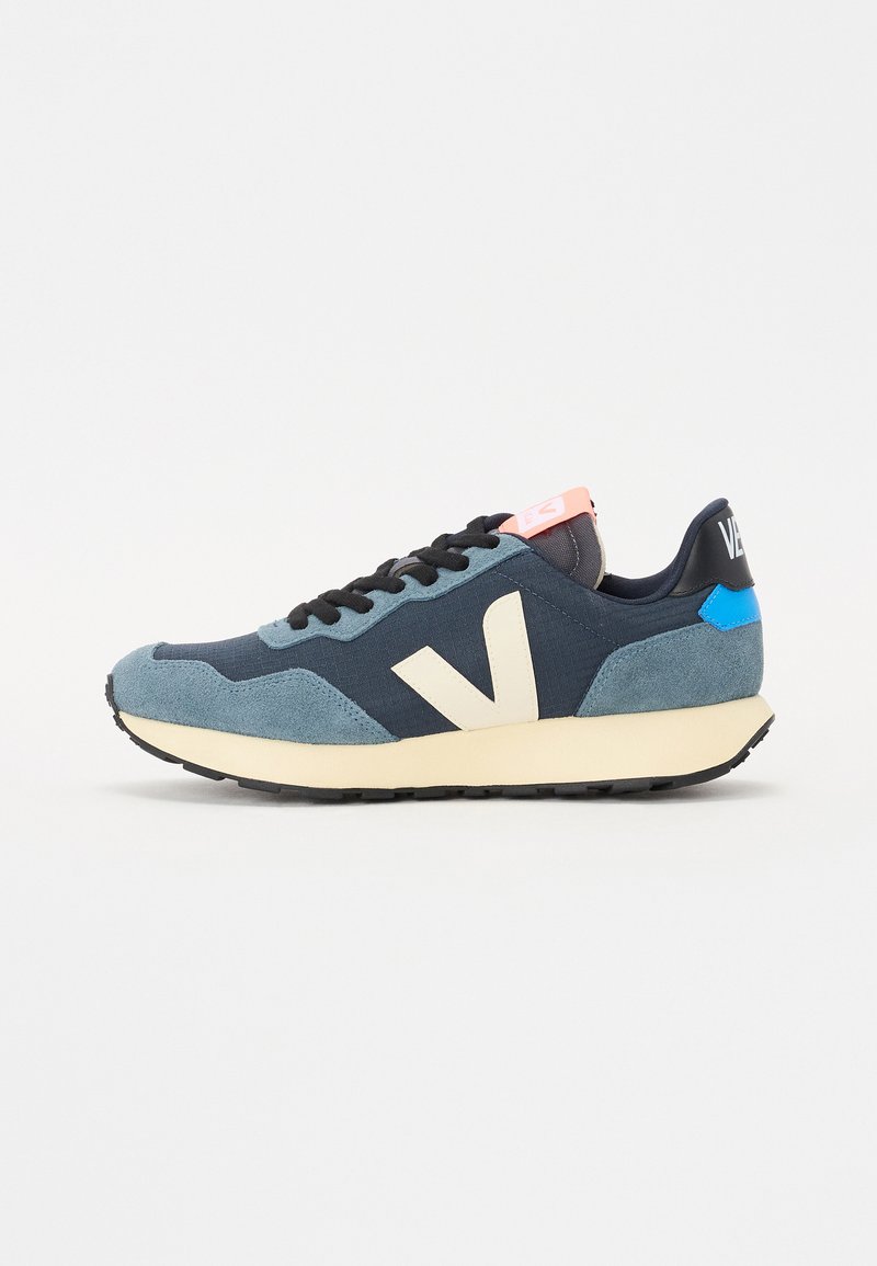 Marineblå og teal sued sneakers med en kremfarget logo, svarte snøringer, og rosa detaljer på tungen. Har en teksturert gummisåle.