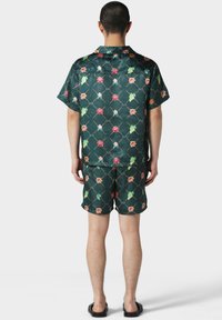 Camisa de manga corta de color verde con un diseño floral y pantalones cortos a juego, hechos de tela suave. Los acentos incluyen flores rosas y naranjas con hojas verdes.