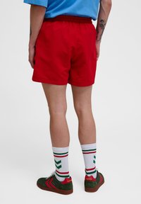 Röda shorts med ett elastiskt midjeband, bärs med vita strumpor som har gröna och röda ränder, och gröna sneakers med röda detaljer.
