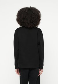 Μαύρο φούτερ με άνετη εφαρμογή, υφή με ζάρες, στρογγυλή λαιμόκοψη και μακριά μανίκια, σε συνδυασμό με ψηλόμεσα μαύρα τζιν.