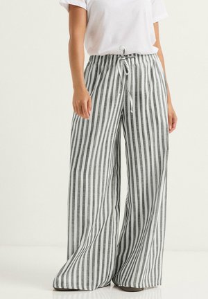 Vrouw draagt losse, hooggetailleerde broek met verticale zwart-witte strepen en een gebonden trekkoord, gecombineerd met een eenvoudig wit T-shirt.